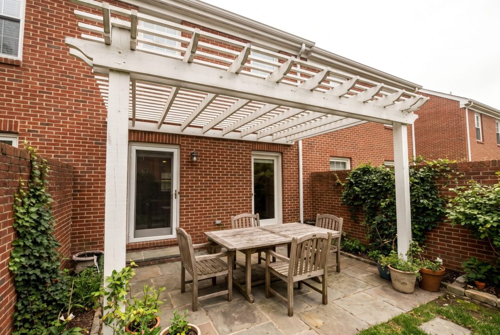 White pergola attached to a brick house over a patio